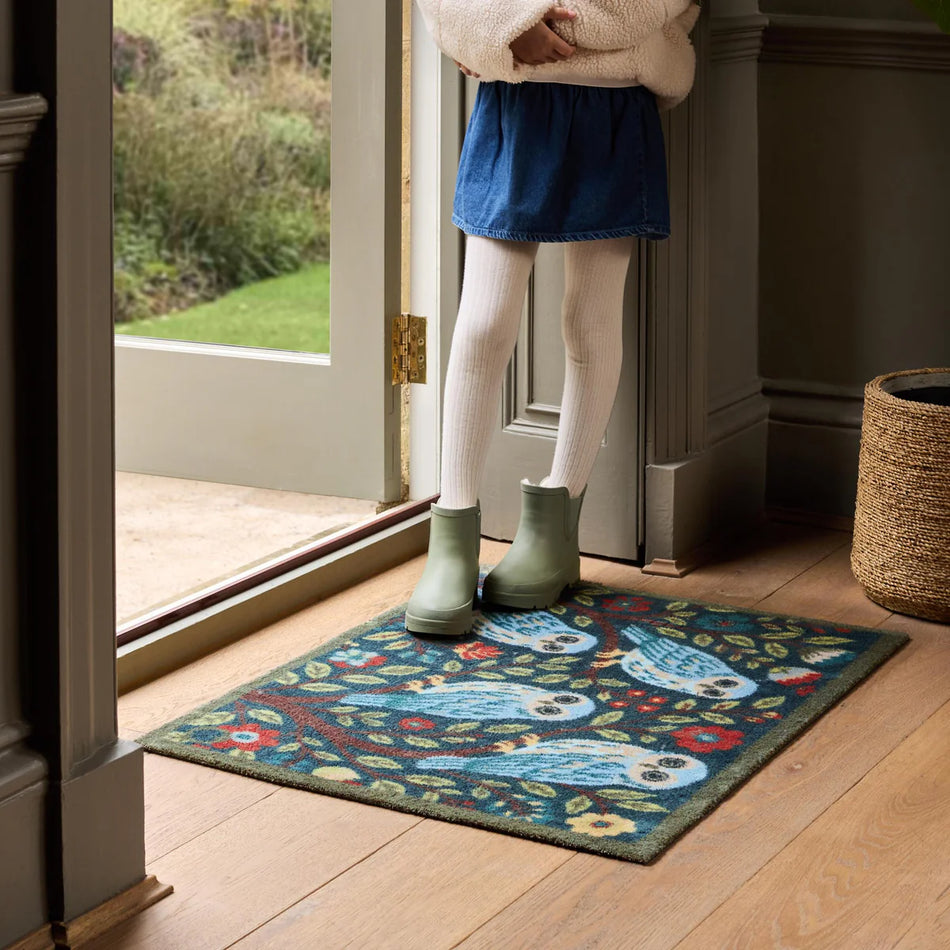 Person wearing green boots stepping onto a decorative doormat with a blue whale design.