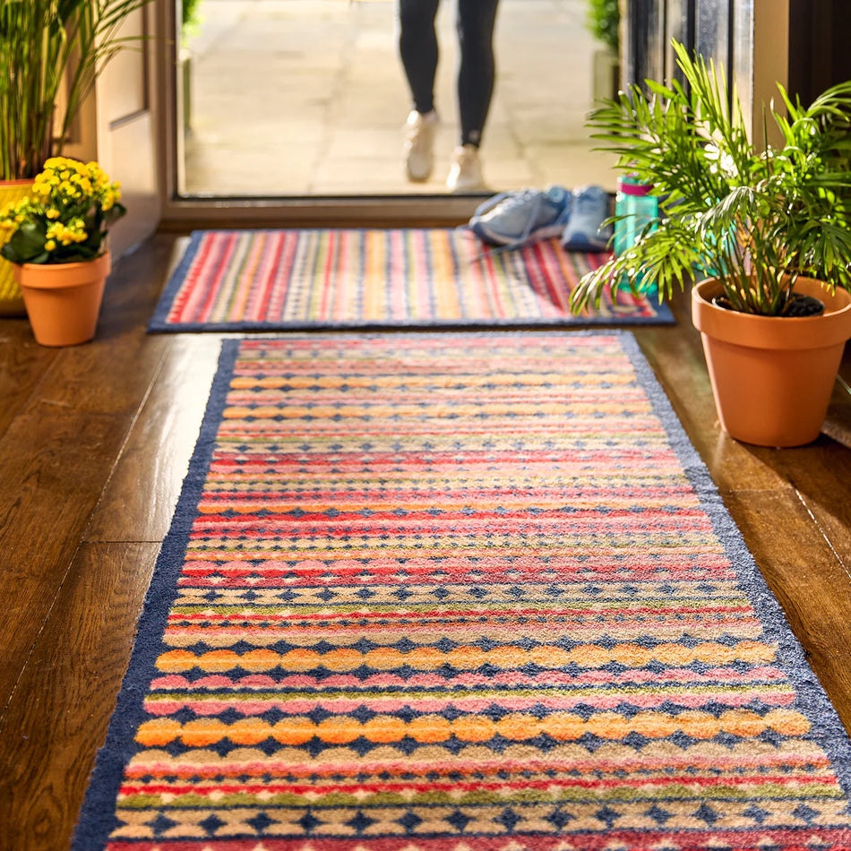 Colorful patterned rug on a wooden floor with potted plants and a person in the background.