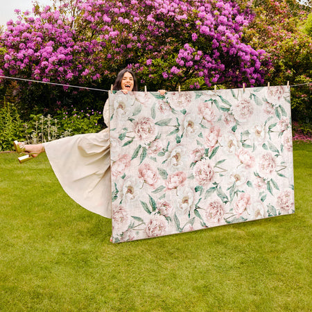 Woman holding a floral blanket in a garden with pink flowers in the background
