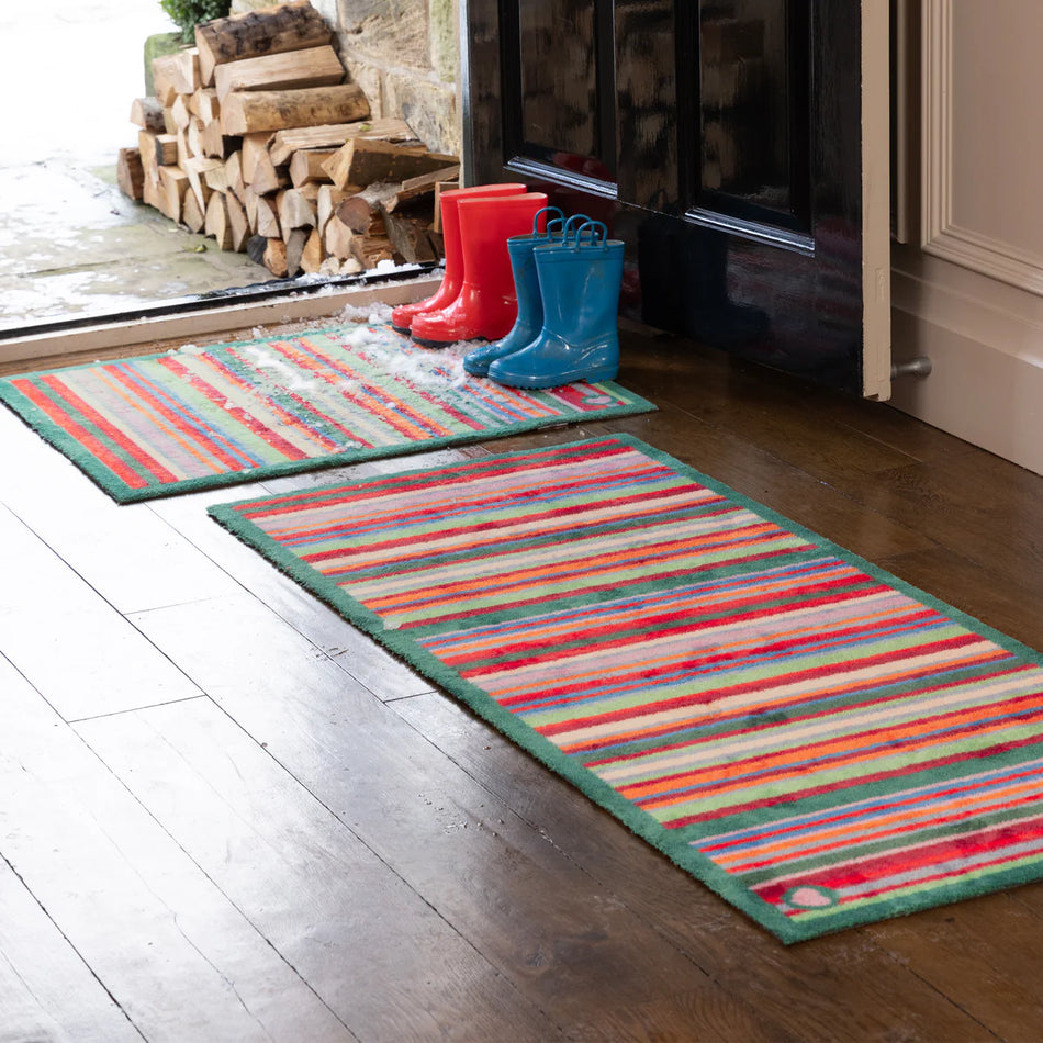Colorful striped rug on a wooden floor with red and blue rain boots near a fireplace.