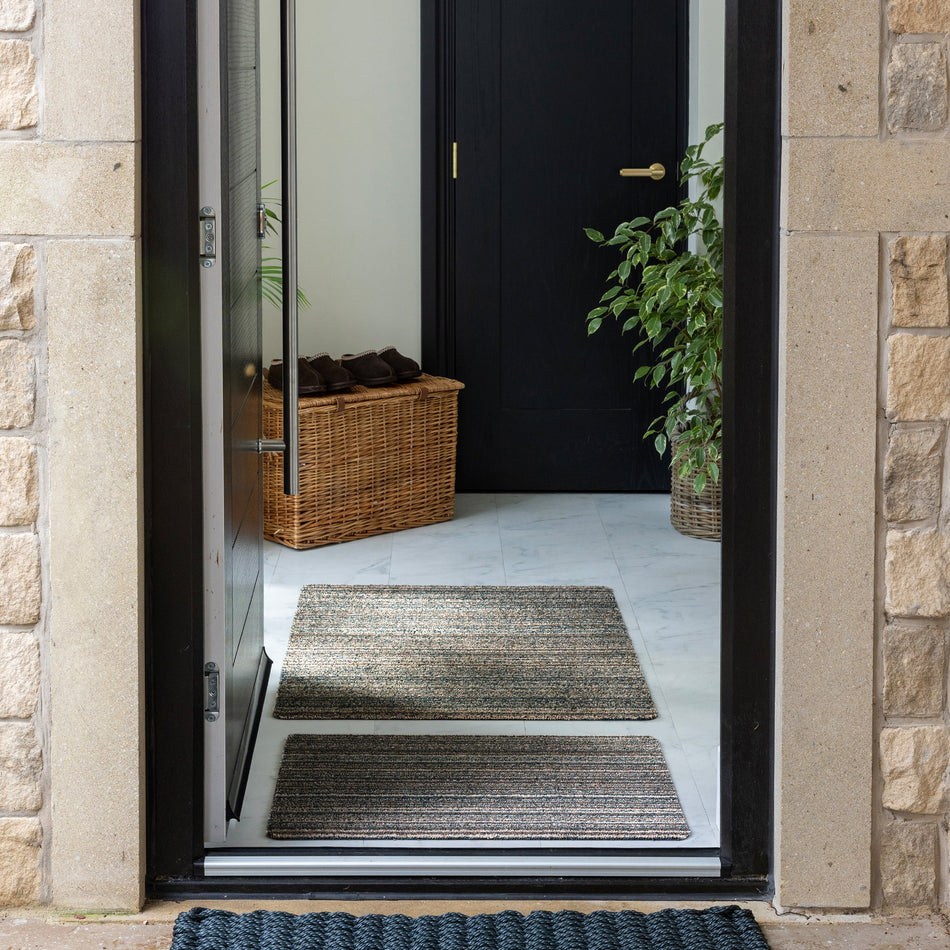 Entryway with two striped doormats on a stone floor, leading to a black door.