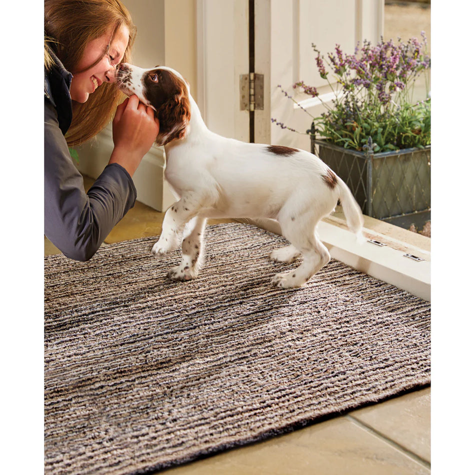 Woman petting a small white dog on a textured rug with a plant in the background