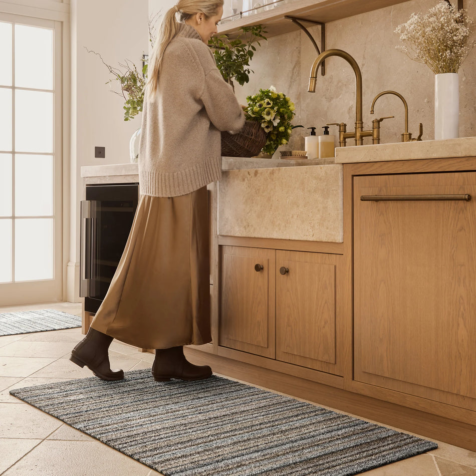 Woman washing dishes in a modern kitchen with wooden cabinets and a large sink.
