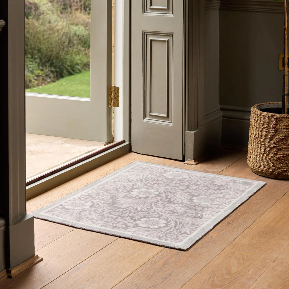Decorative doormat on wooden floor with open door leading to garden