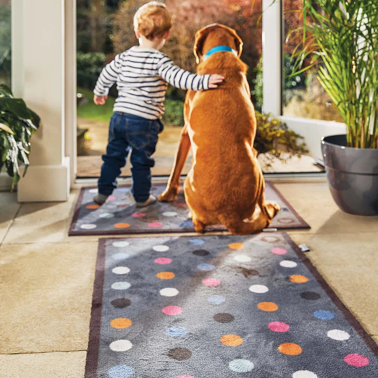 Child and dog standing on a colorful polka dot rug indoors
