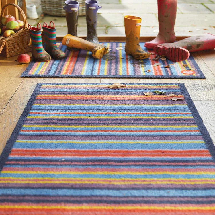 Colorful striped rug with children's wellies and socks on a wooden floor.
