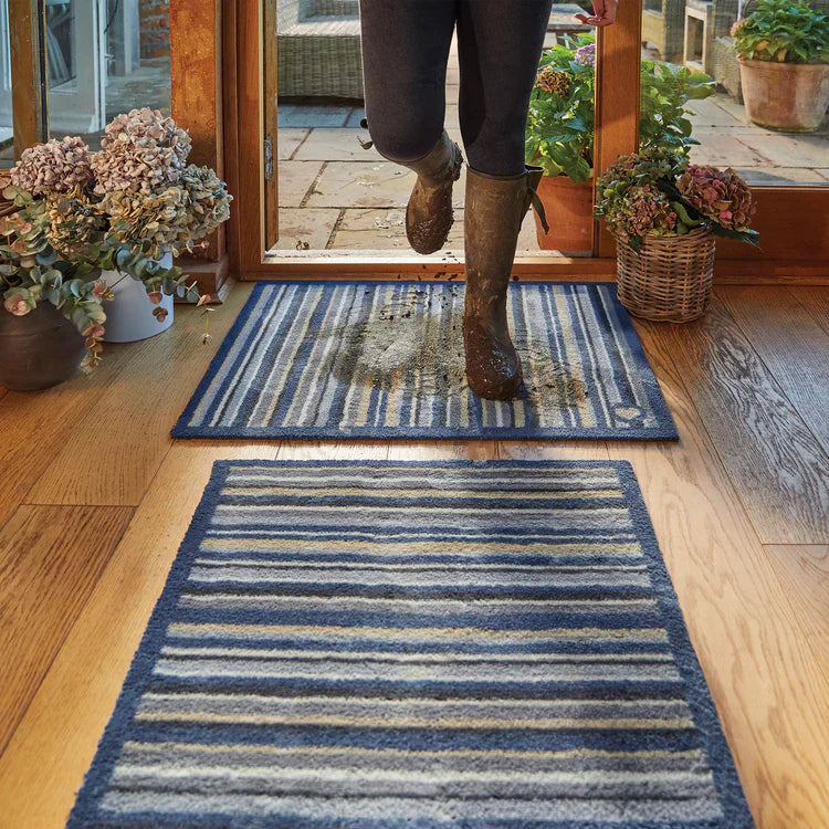 Person stepping onto a blue striped rug from a wooden floor into a patio area.