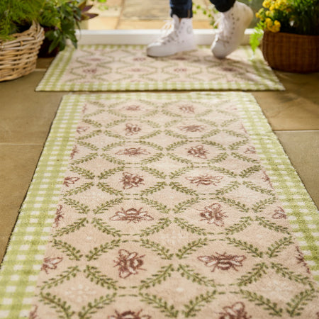 Decorative rug with floral pattern on a wooden floor, with a person wearing white shoes stepping onto it.