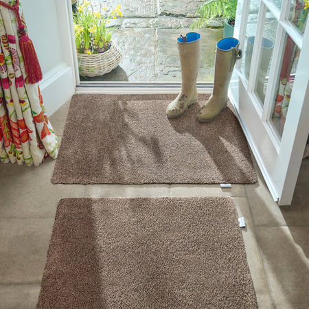Brown door mats in front of a glass door with wellington boots on one mat.