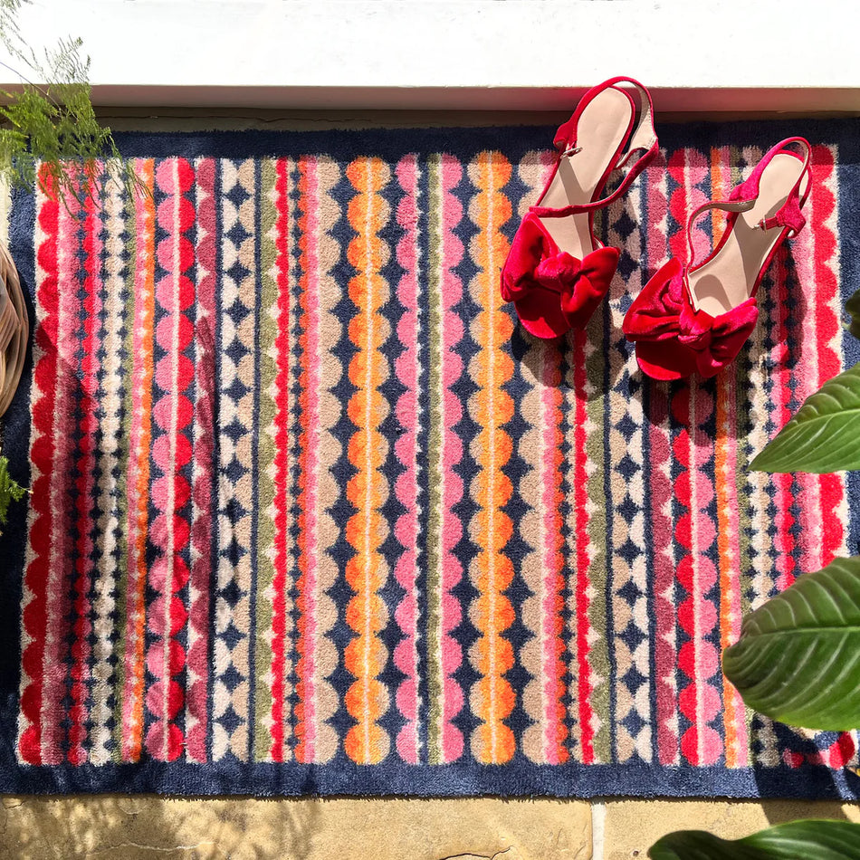 Red high-heeled shoes on a colorful patterned rug with plants on either side.