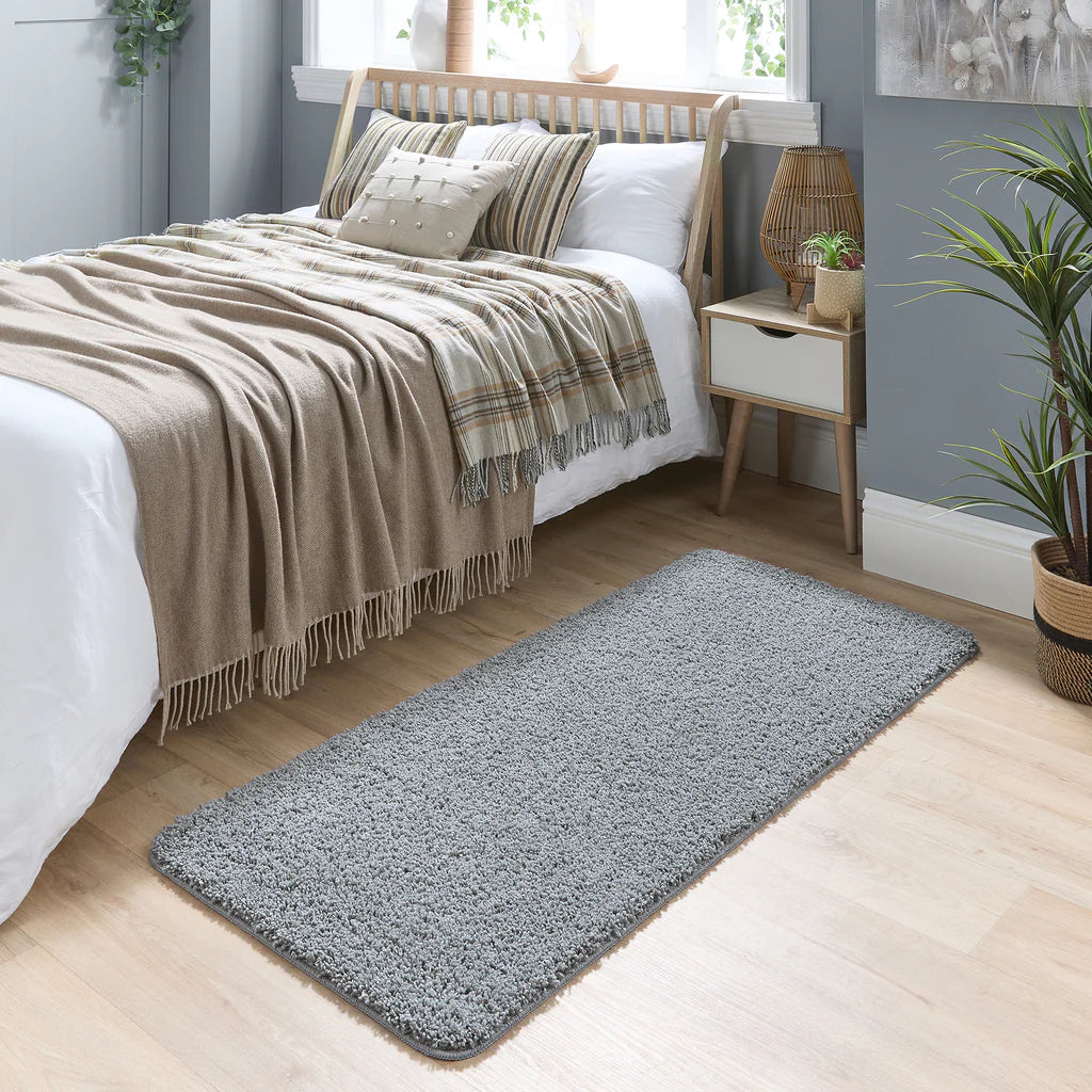 Blue Fleck rug on a wooden floor in a bedroom with a bed and nightstand.