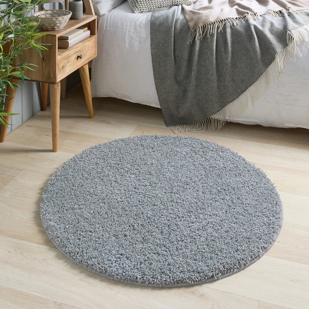 Round Blue Fleck rug on a wooden floor with a bed and side table in the background
