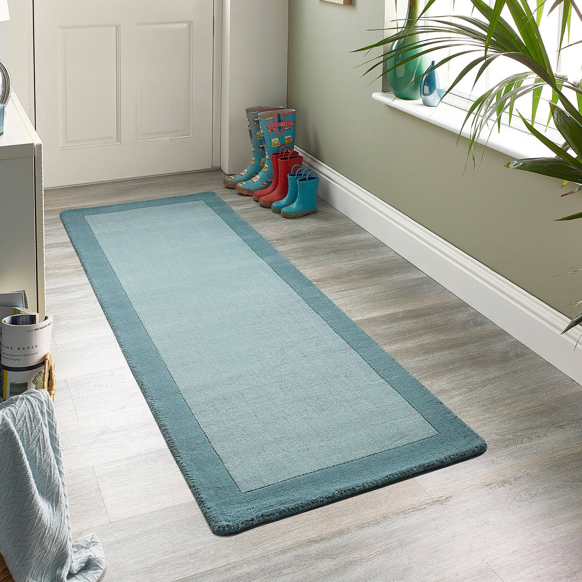 Long blue runner rug on a wooden floor with colorful boots and a plant in the background.
