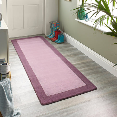 Pink runner rug on a wooden floor with colorful boots and a plant in the background.