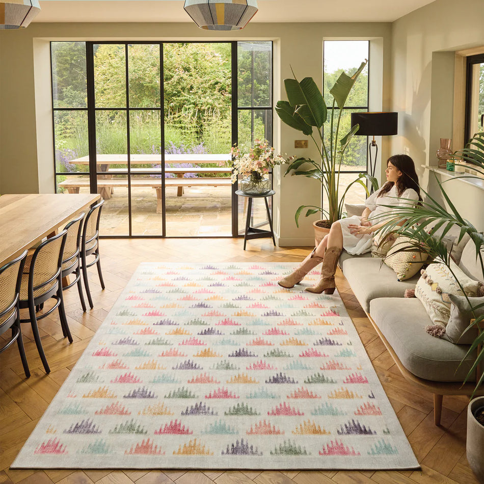 Woman sitting on a couch in a modern living room with a colorful rug.