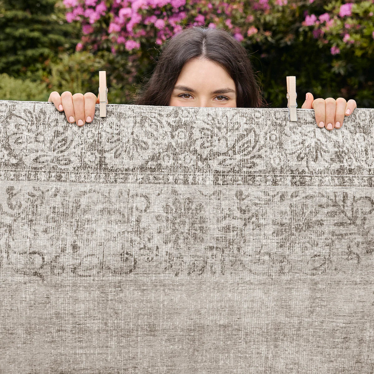Person holding a patterned rug with pink flowers in the background