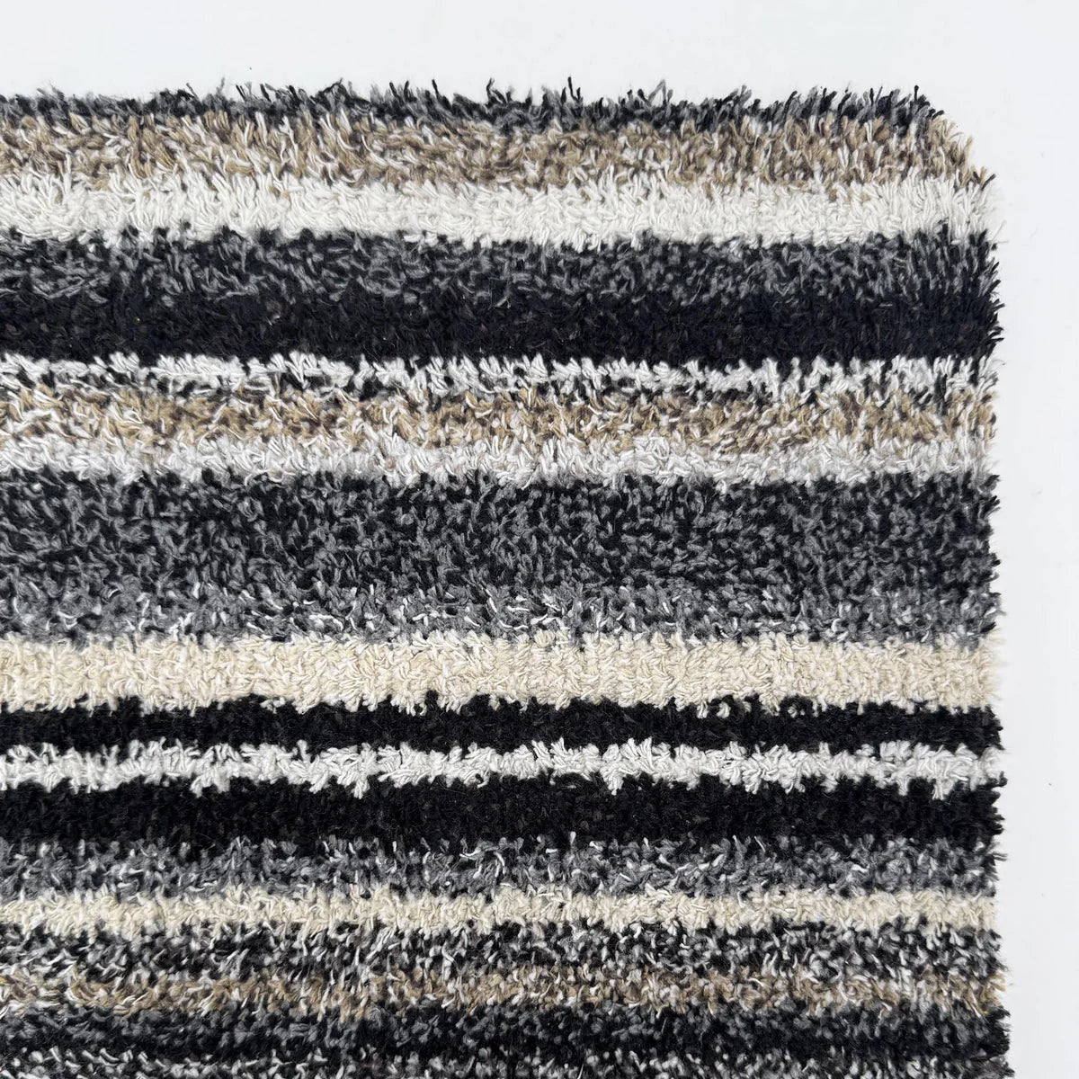 Striped shaggy rug with black, gray, and beige colors on a white background