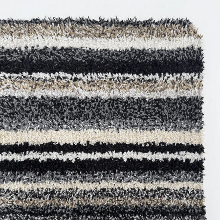 Striped shaggy rug with black, gray, and beige colors on a white background