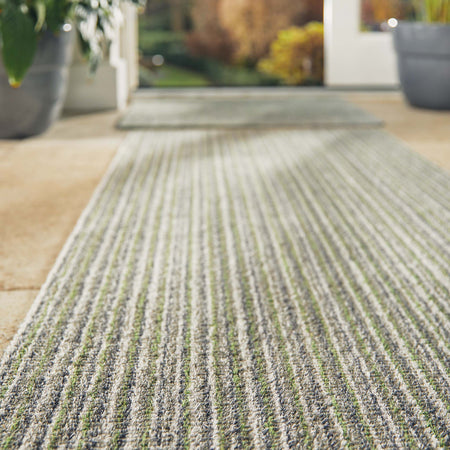 Close-up of a textured green and gray rug with potted plants in the background.