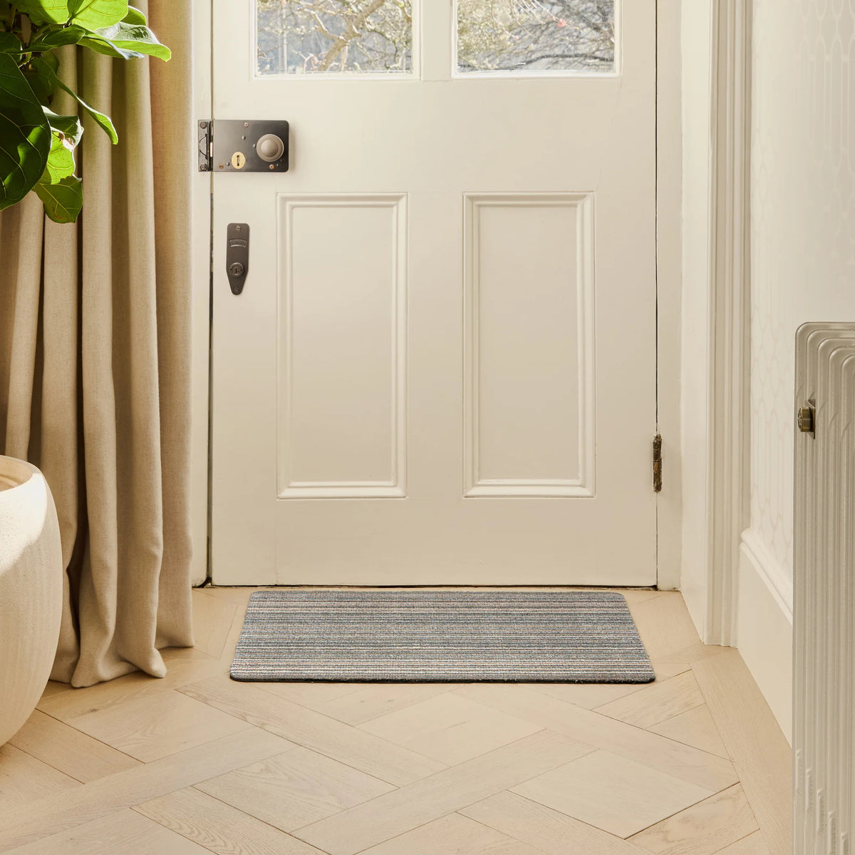 White door with a doormat on a tiled floor, plant to the left