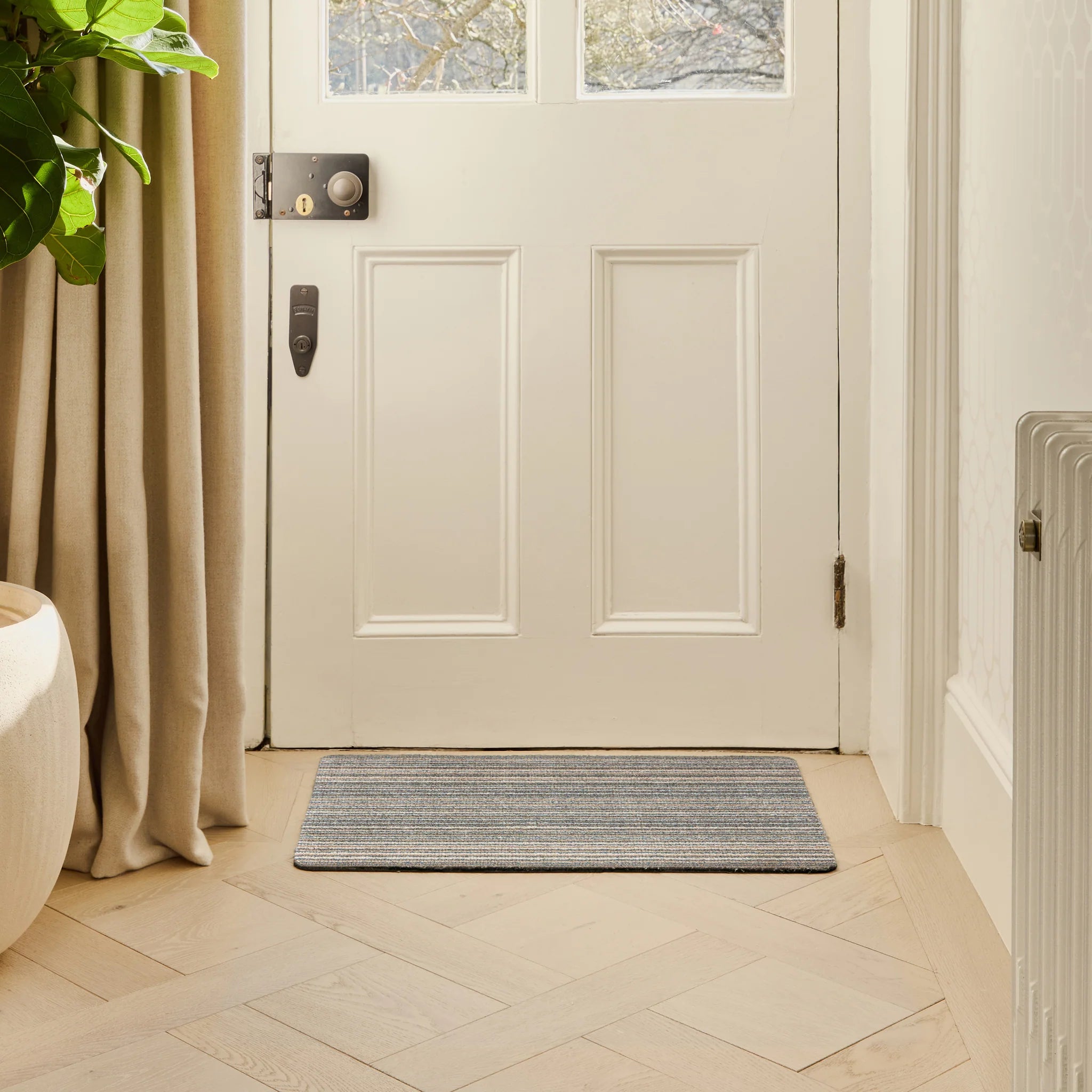 White door with a doormat on a tiled floor, plant to the left