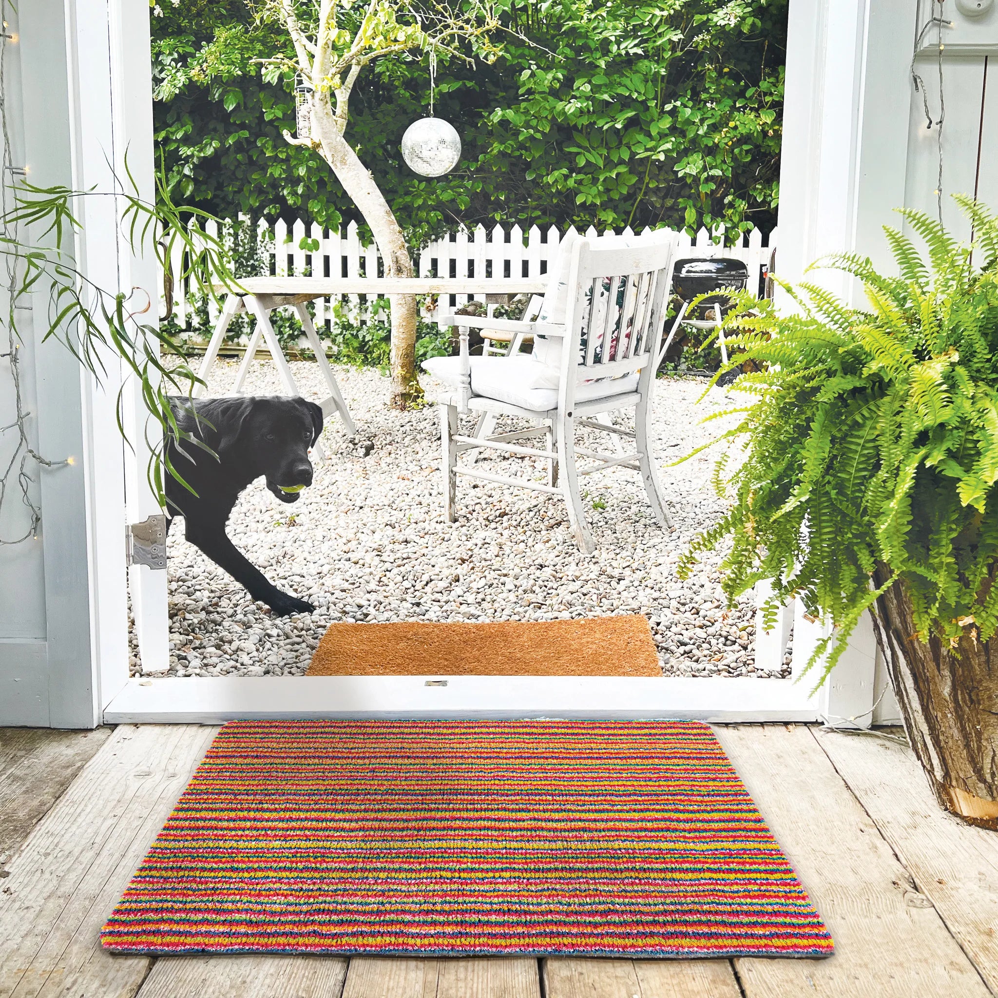 Multicolored doormat on a wooden floor with a garden view through a glass door.