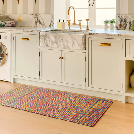 Colorful rug on a wooden floor in a kitchen with marble island and gold fixtures.