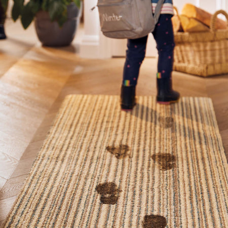 Person wearing rain boots stepping onto a doormat with paw prints, carrying a bag labeled 'Winter'.