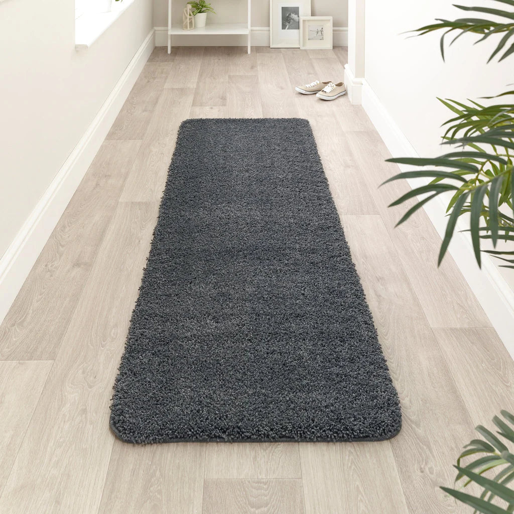 Long dark gray rug on a light wooden floor with a plant in the corner.