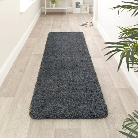 Long dark gray rug on a light wooden floor with a plant in the corner.