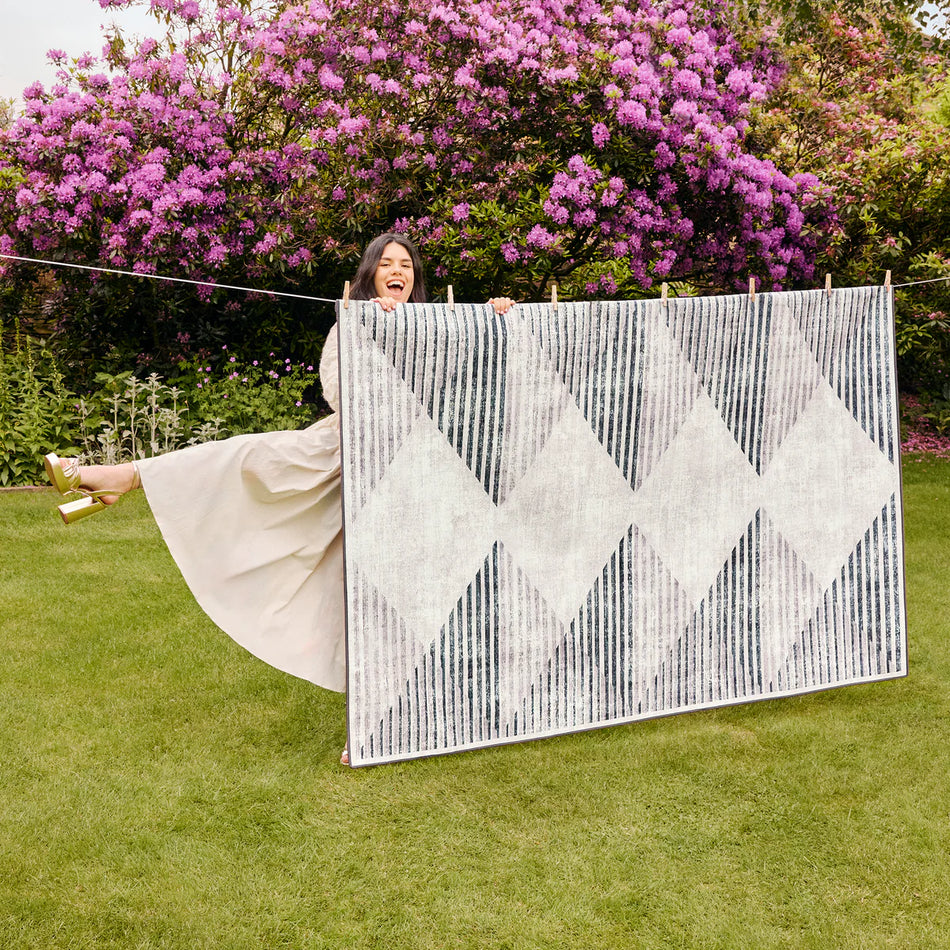 Woman holding a large woven wall art piece outdoors with purple flowers in the background