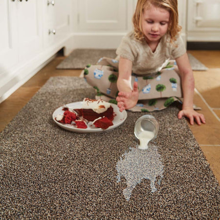 Child in a kitchen with a plate of cake and spilled milk on a carpeted floor.