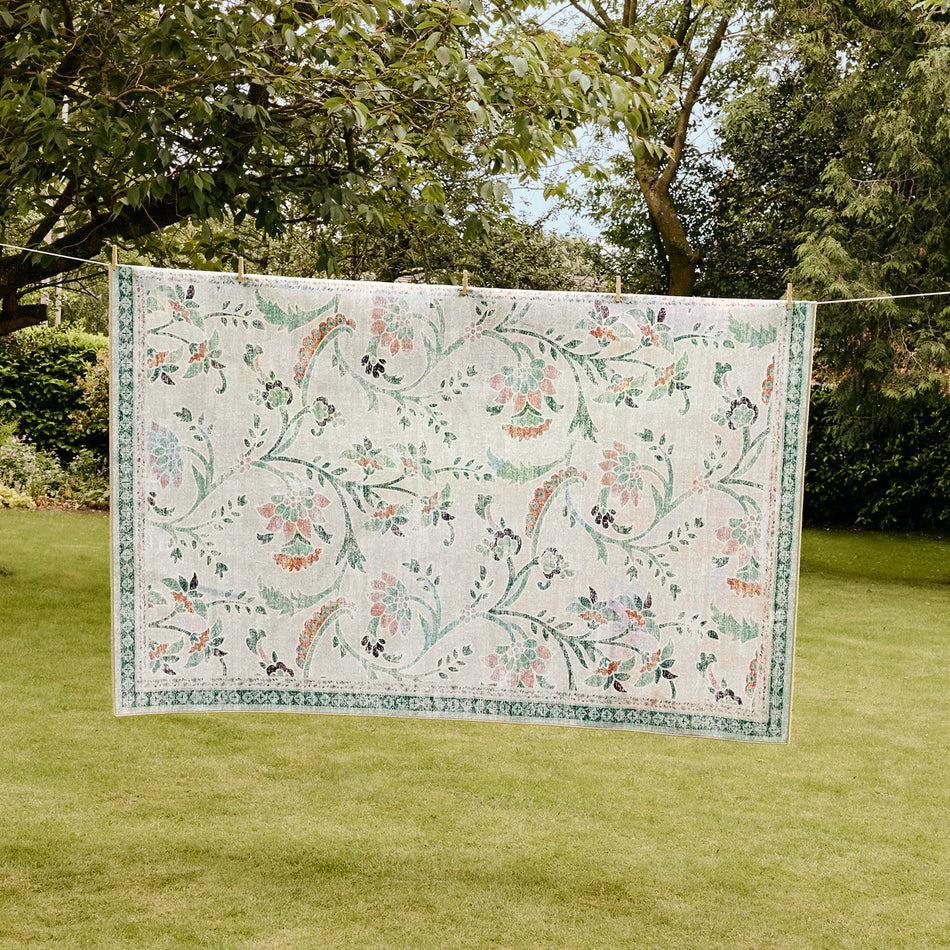 Floral-patterned rug on a grassy area with trees in the background