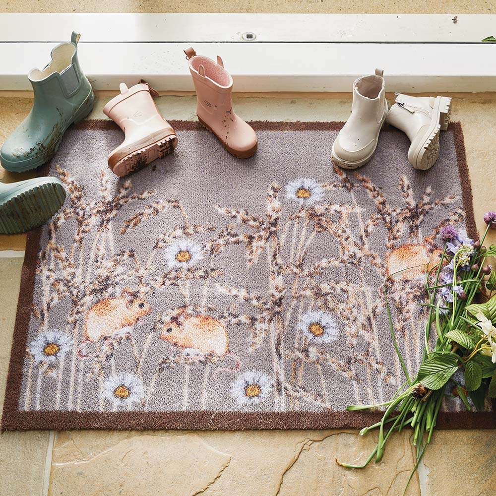 Decorative doormat with floral pattern on a floor with boots around it