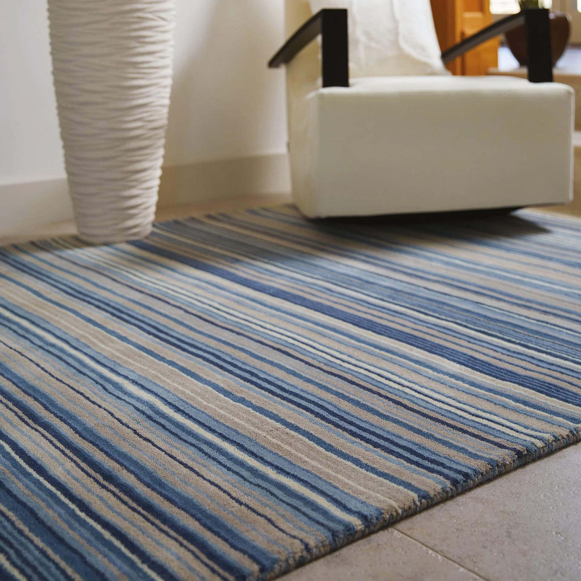 origins Striped blue and beige rug in a room with a white chair and wicker basket.