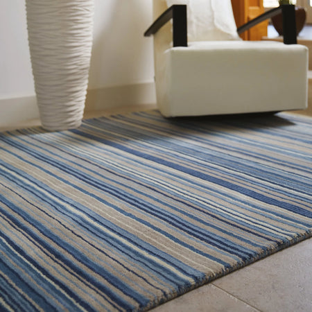 origins Striped blue and beige rug in a room with a white chair and wicker basket.