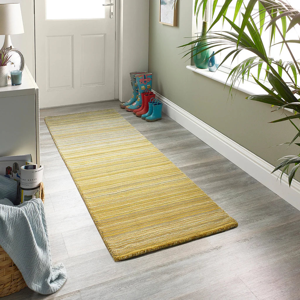 Yellow runner rug on a wooden floor with colorful boots and a plant in the background.
