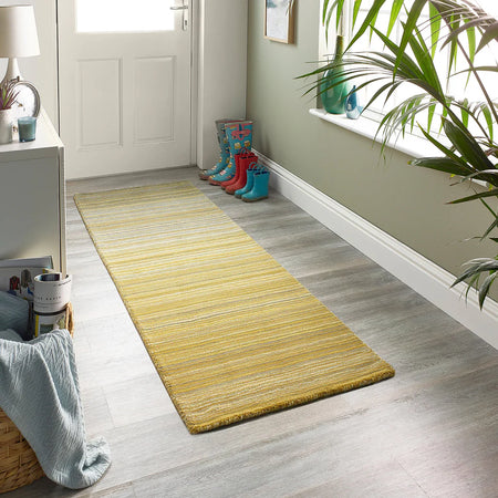 Yellow runner rug on a wooden floor with colorful boots and a plant in the background.