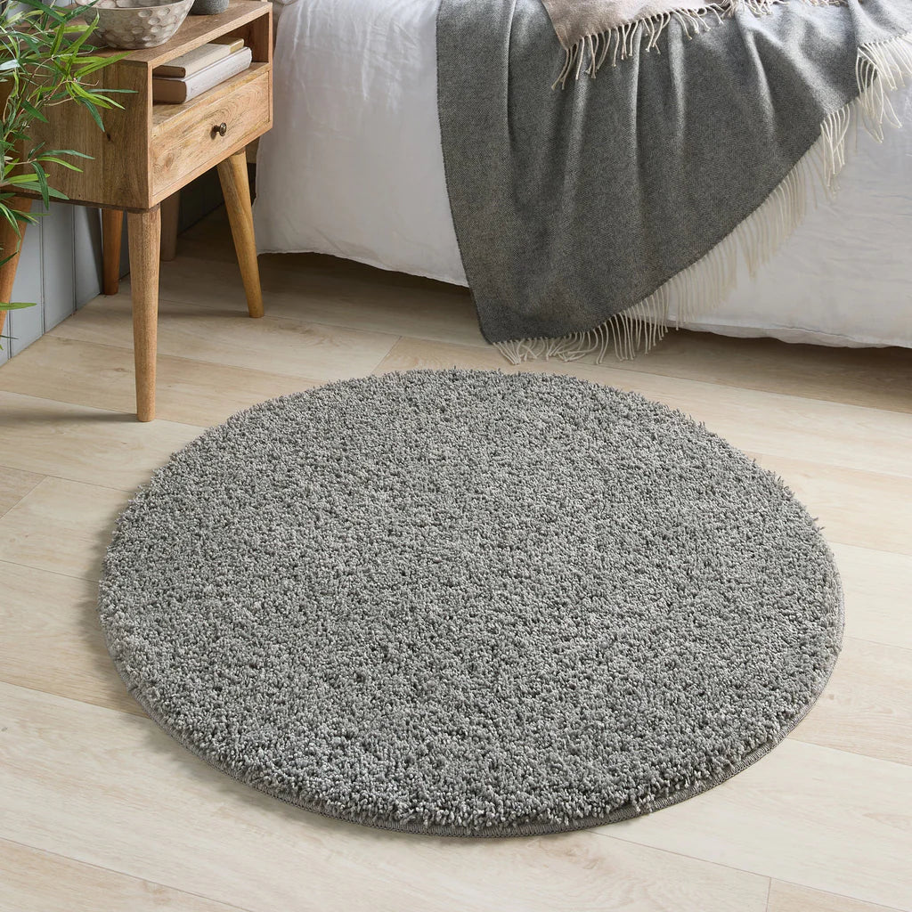 Round grey rug on a wooden floor in a bedroom setting.