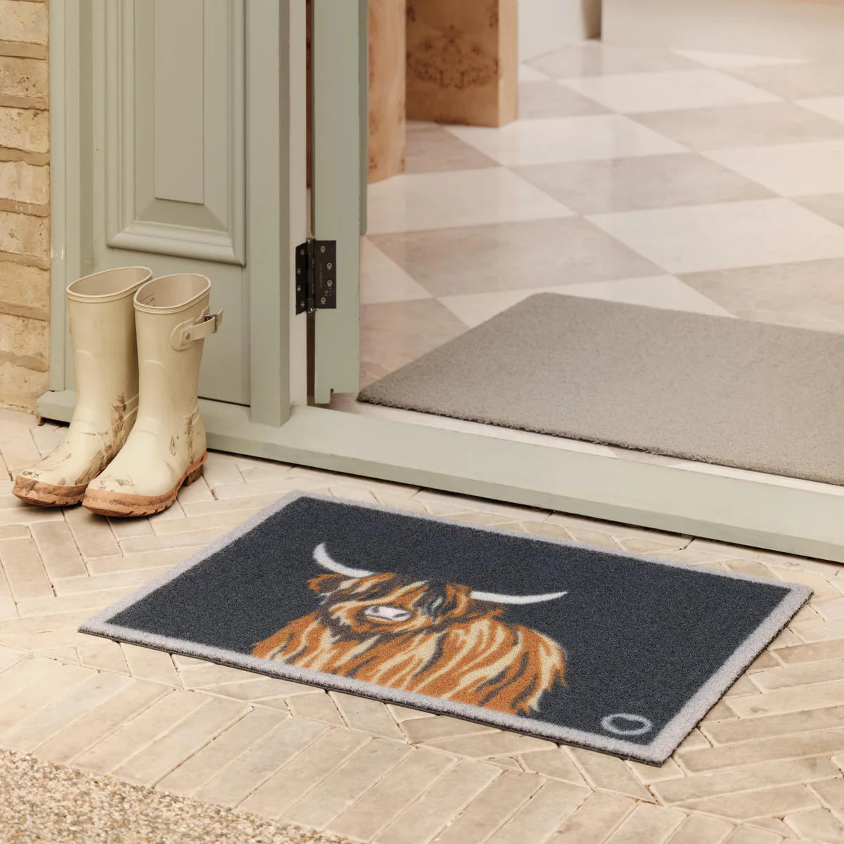 Doormat with a highland cow design on a tiled floor outside a door.