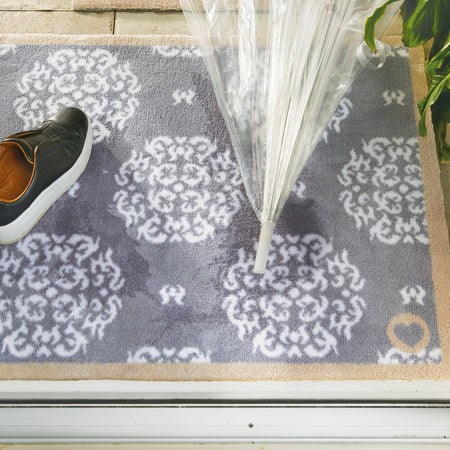 Gray doormat with white patterns on a wooden floor, next to a shoe and an umbrella.