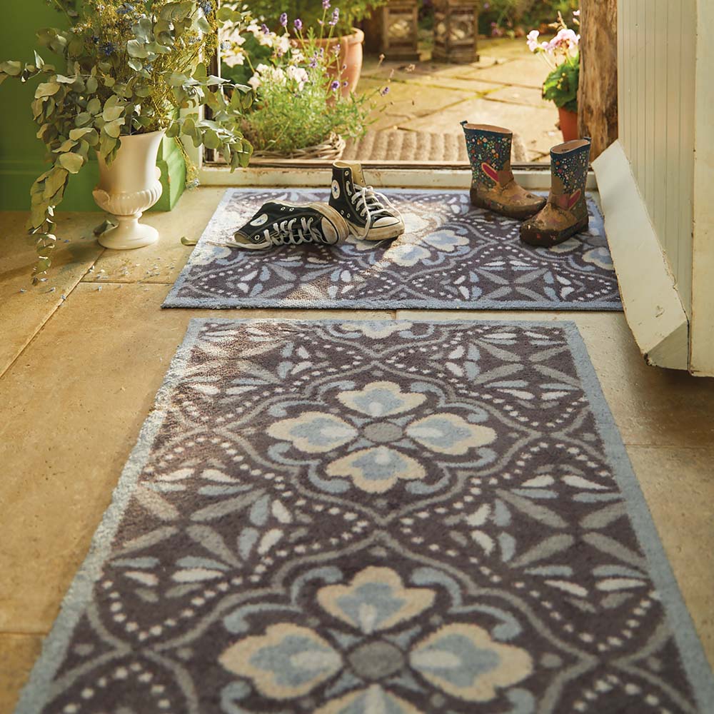 Decorative rug with floral pattern on a patio with boots and plants.