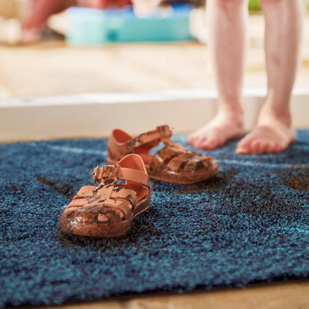 Brown sandals on a blue rug with blurred feet in the background