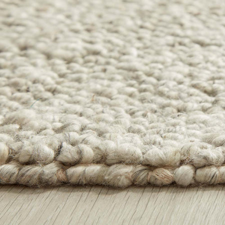 Close-up of a textured beige silver rug on a wooden floor