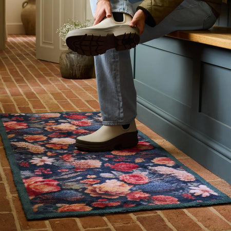 Person putting on a white shoe with black sole on a floral rug.