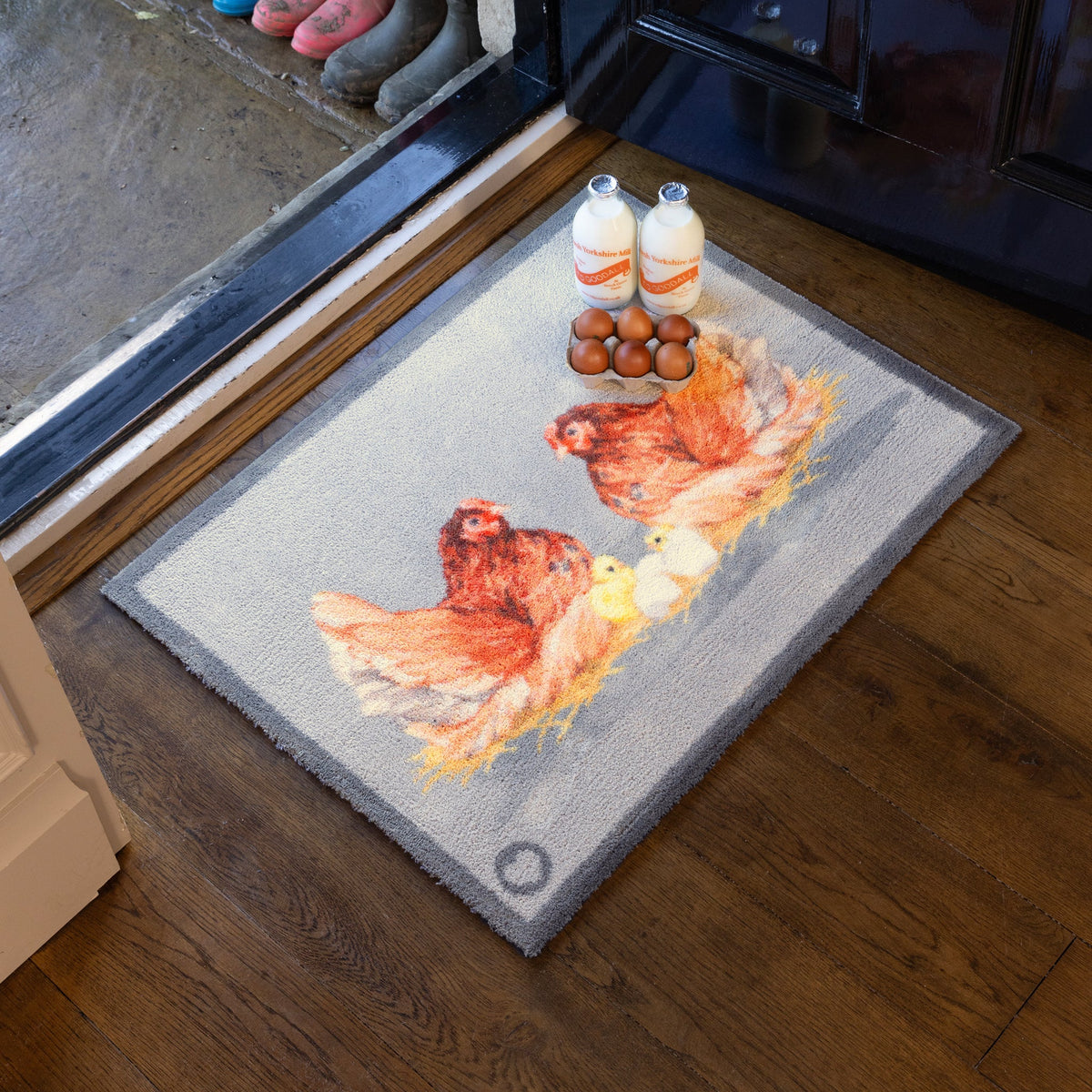 Decorative doormat with chicken design on a wooden floor.