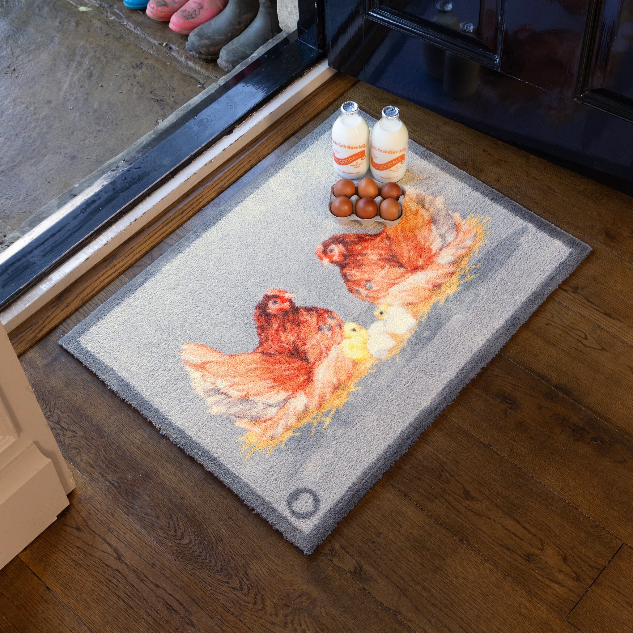 Decorative doormat with chicken design on a wooden floor.