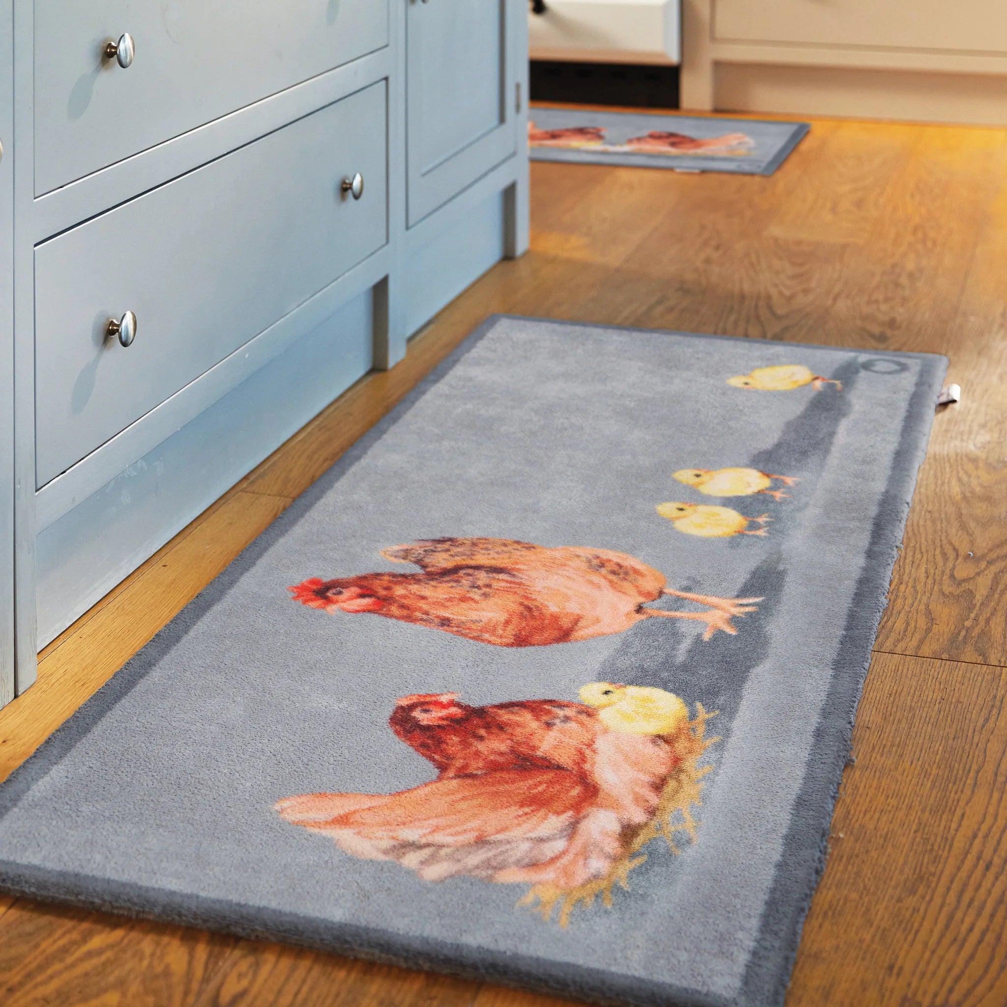 Gray rug with chicken design on a wooden floor next to a blue cabinet.