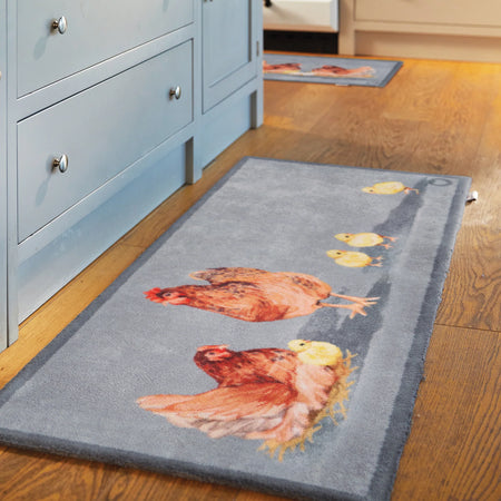 Gray rug with chicken design on a wooden floor next to a blue cabinet.