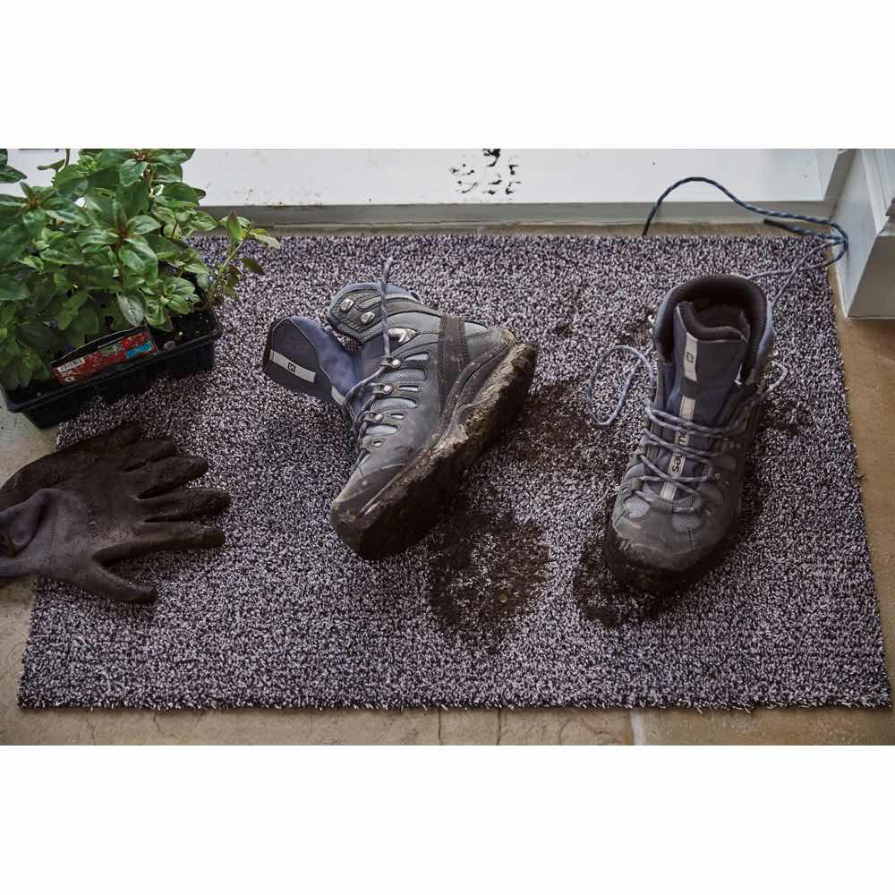 Wet shoes and gloves on a doormat with water droplets, indicating recent rain.